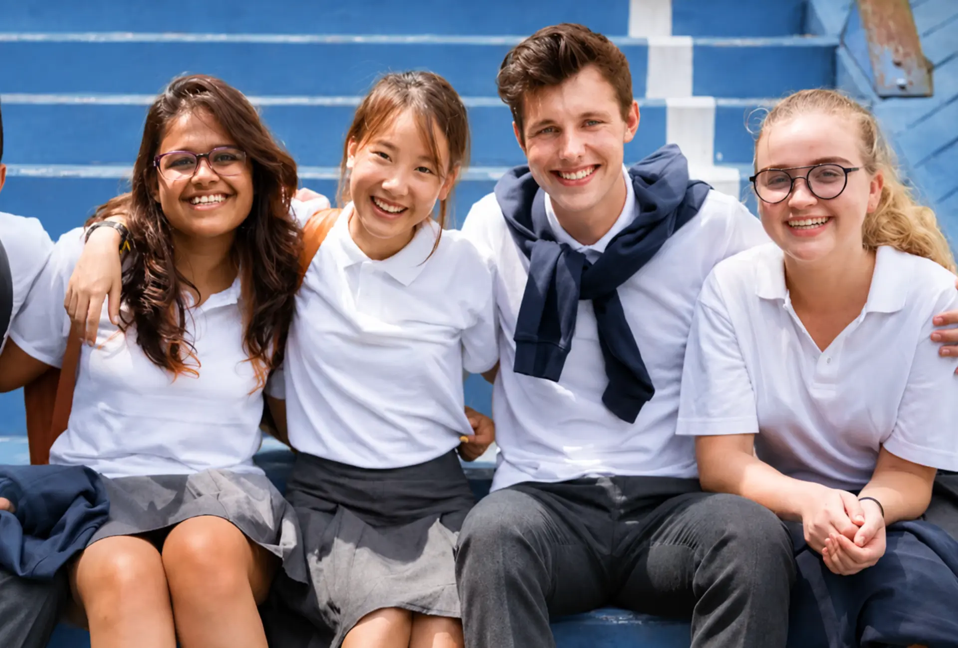 High school students in white uniforms sitting together on blue bleachers